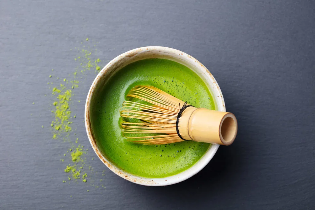 Matcha green tea powder in a bowl, being whisked with a wooden whisk. A traditional Japanese beverage